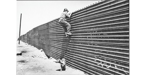 Tijuana, Baja California, 1996. Un trabajador mira por encima del muro entre México y Estados Unidos. Cuando la Patrulla fronteriza no esté observando podrá cruzar por debajo de la cerca. Foto: David Bacon